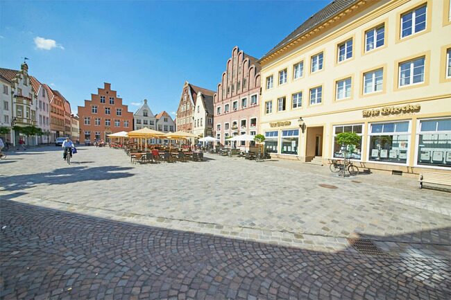 A wide view of Warendorf’s market square featuring cobblestone pavement, historic colorful buildings, outdoor cafes with umbrellas, and a clear blue sky.
